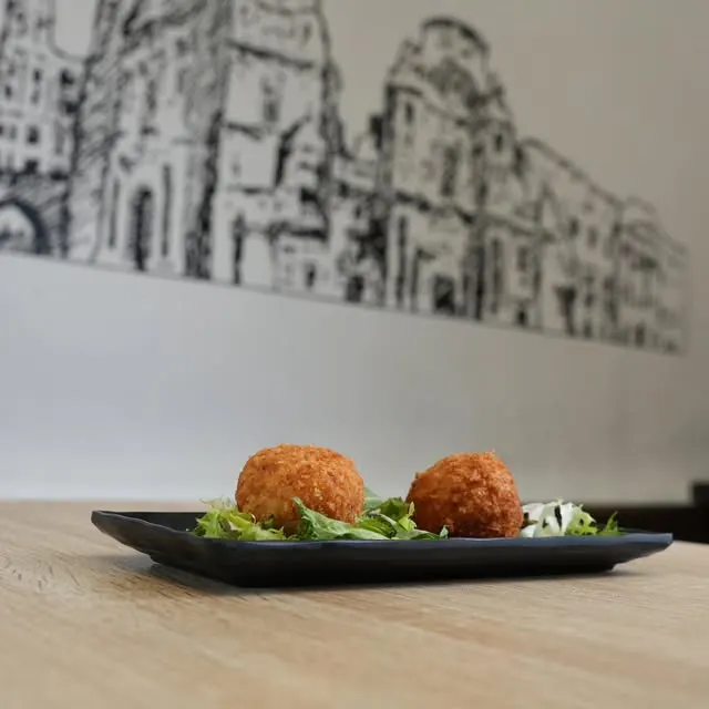 Dos croquetas sobre lechuga en una fuente negra, en una mesa de madera de La Tapa de San Lorenzo